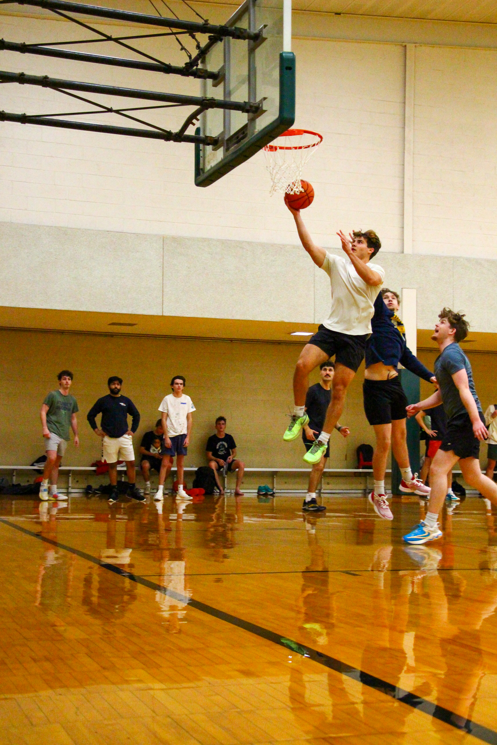 A young man jumps to make a basketball shot during a game as others look from the sidelines.