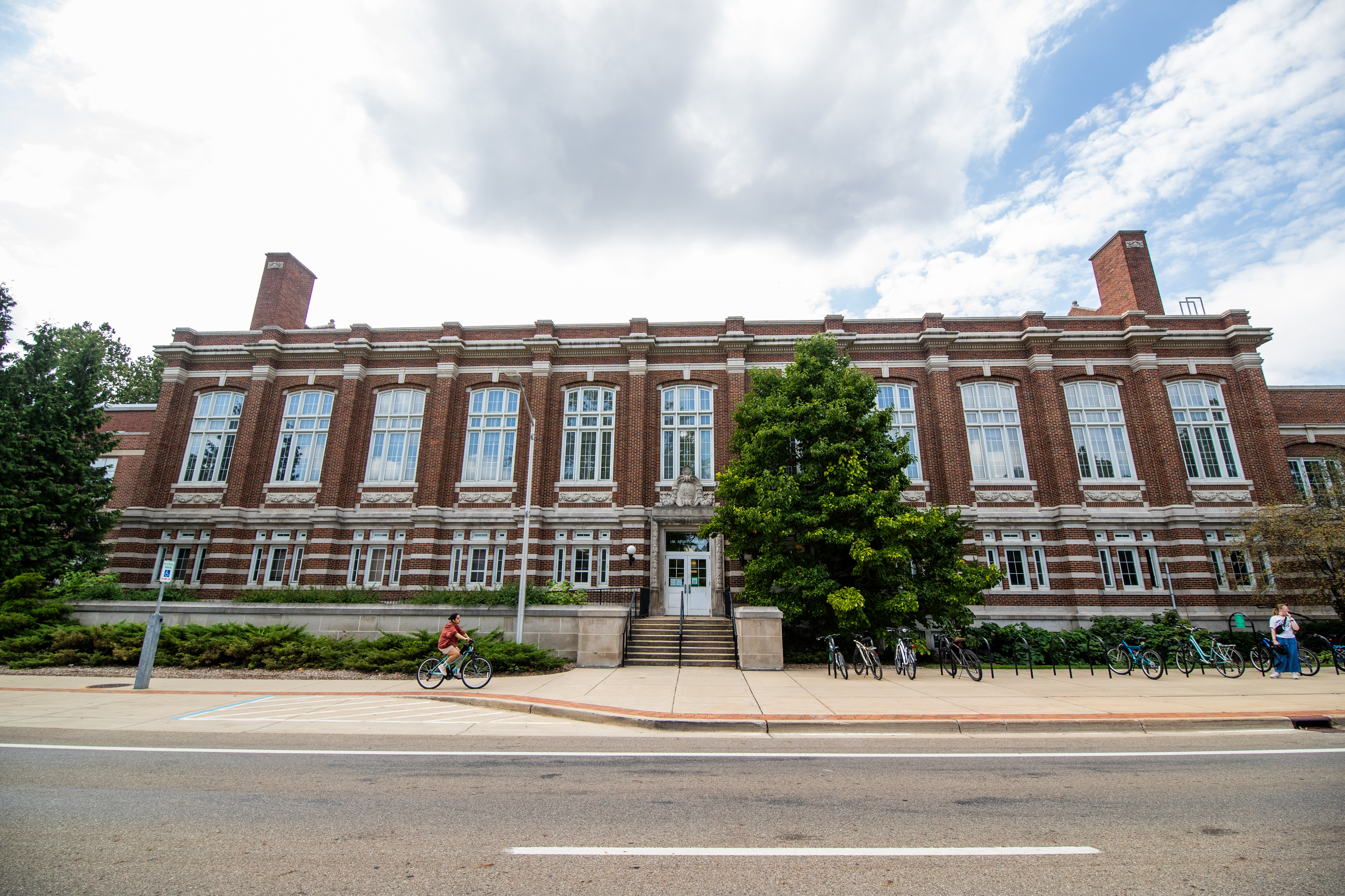A historic brick building, IM Circle, is shown with a biker riding on the sidewalk in front.