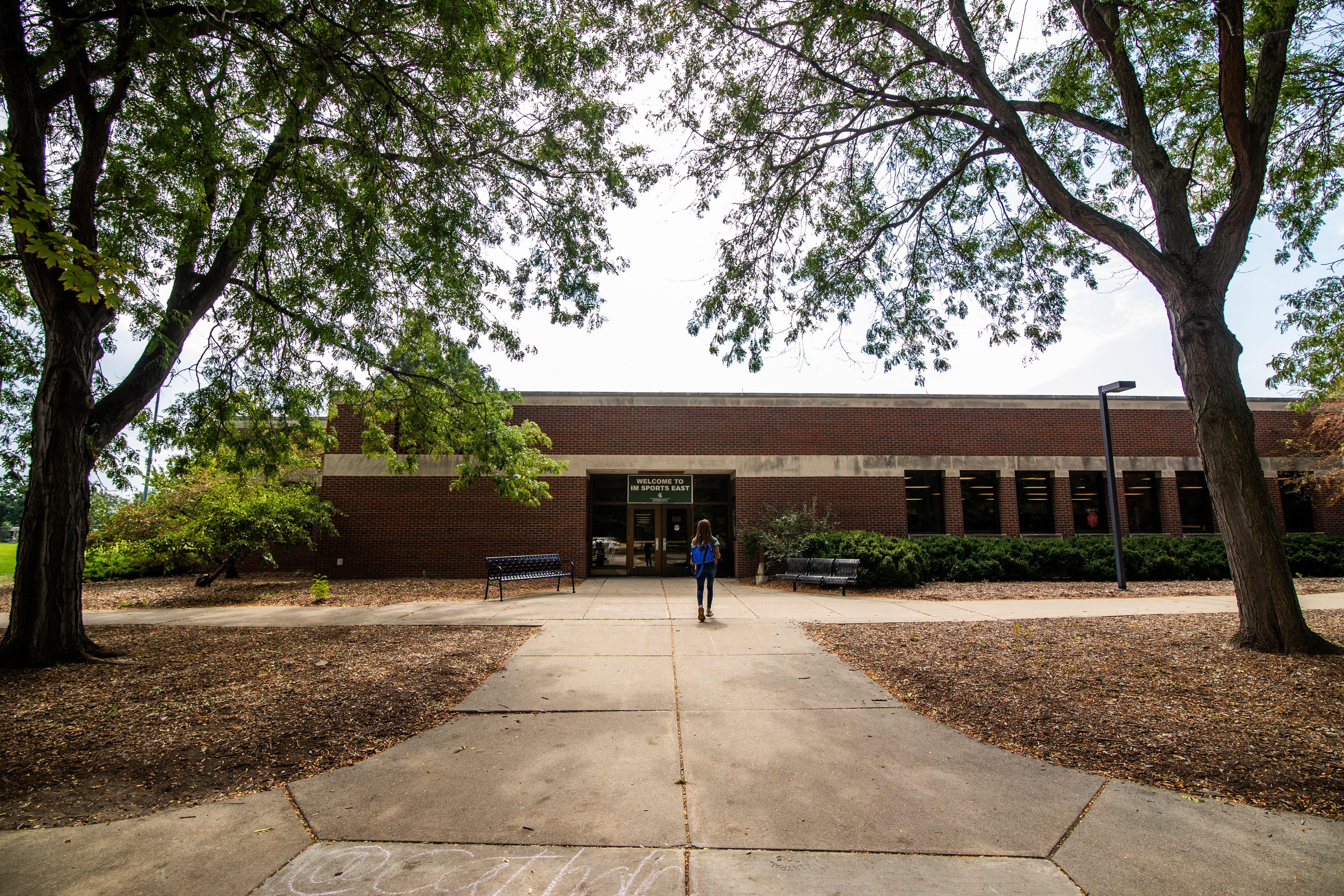 Straight-on view of IM East building, as a student walks toward the door.